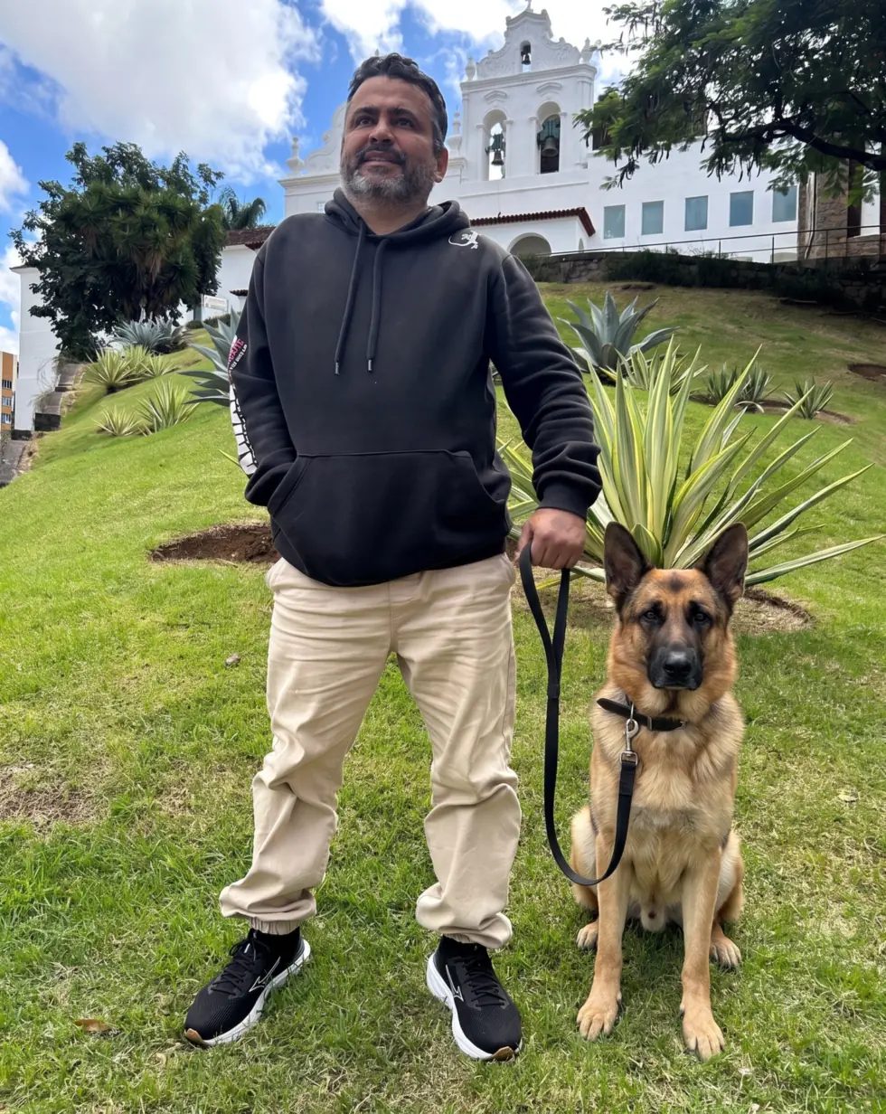 V. Júnior, especialista em comportamento canino na Grande Vitória, de pé segurando a guia de um pastor alemão sentado em posição de junto